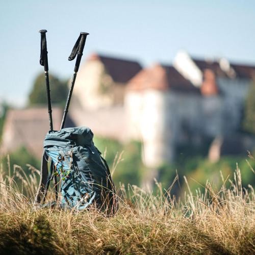Rucksack und Wanderstöcke im Hintergrund verschwommenes Schloss, Foto: niclasnomis media