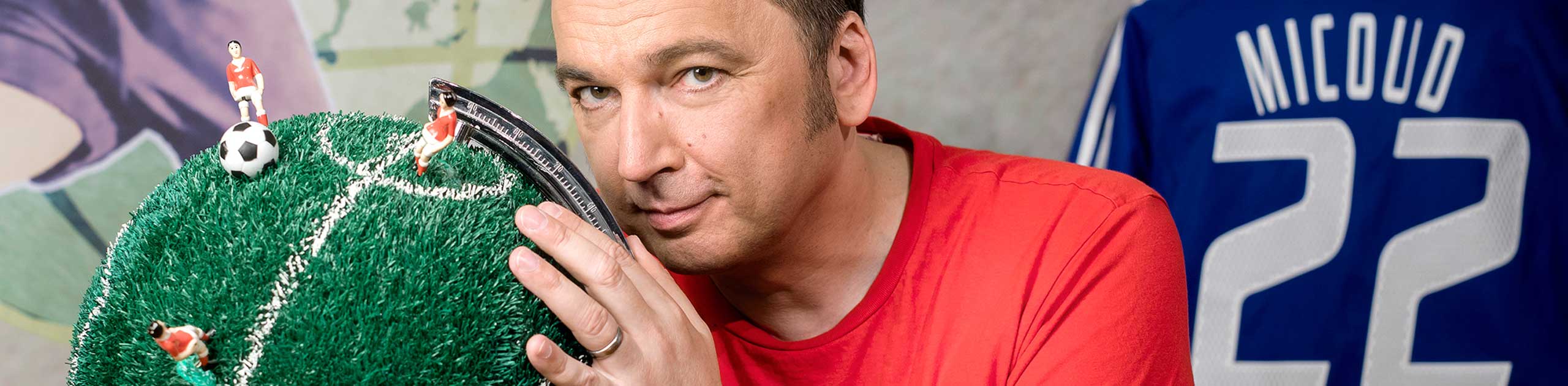 Mann mit rotem T-Shirt, Globus als Fußballfeld und blaues Fußballtrikot, Fotocredit WDR